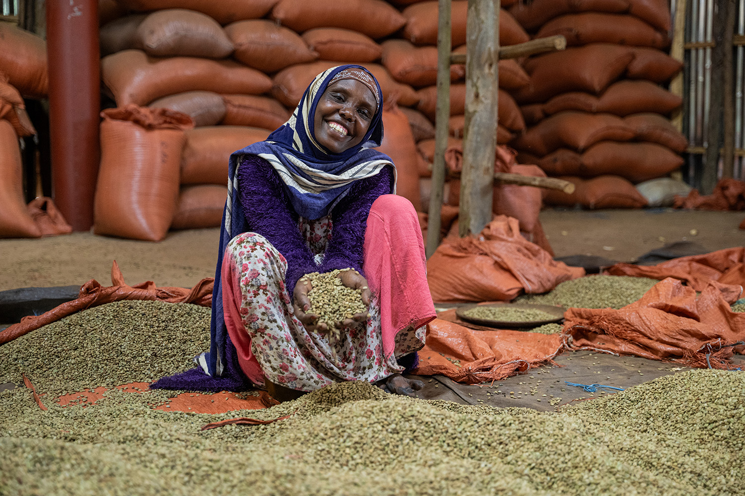 Ethiopian woman sitting in coffee beans with coffee bags in the background