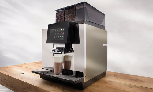 Fully automatic coffee machine with chocolate on a wooden table against a gray background