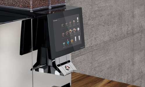Fully automatic coffee machine with coffee beans on a wooden table in front of a gray stone wall
