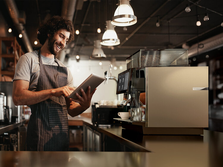 Barista operates tablet while the coffee machine froths milk and brews coffee