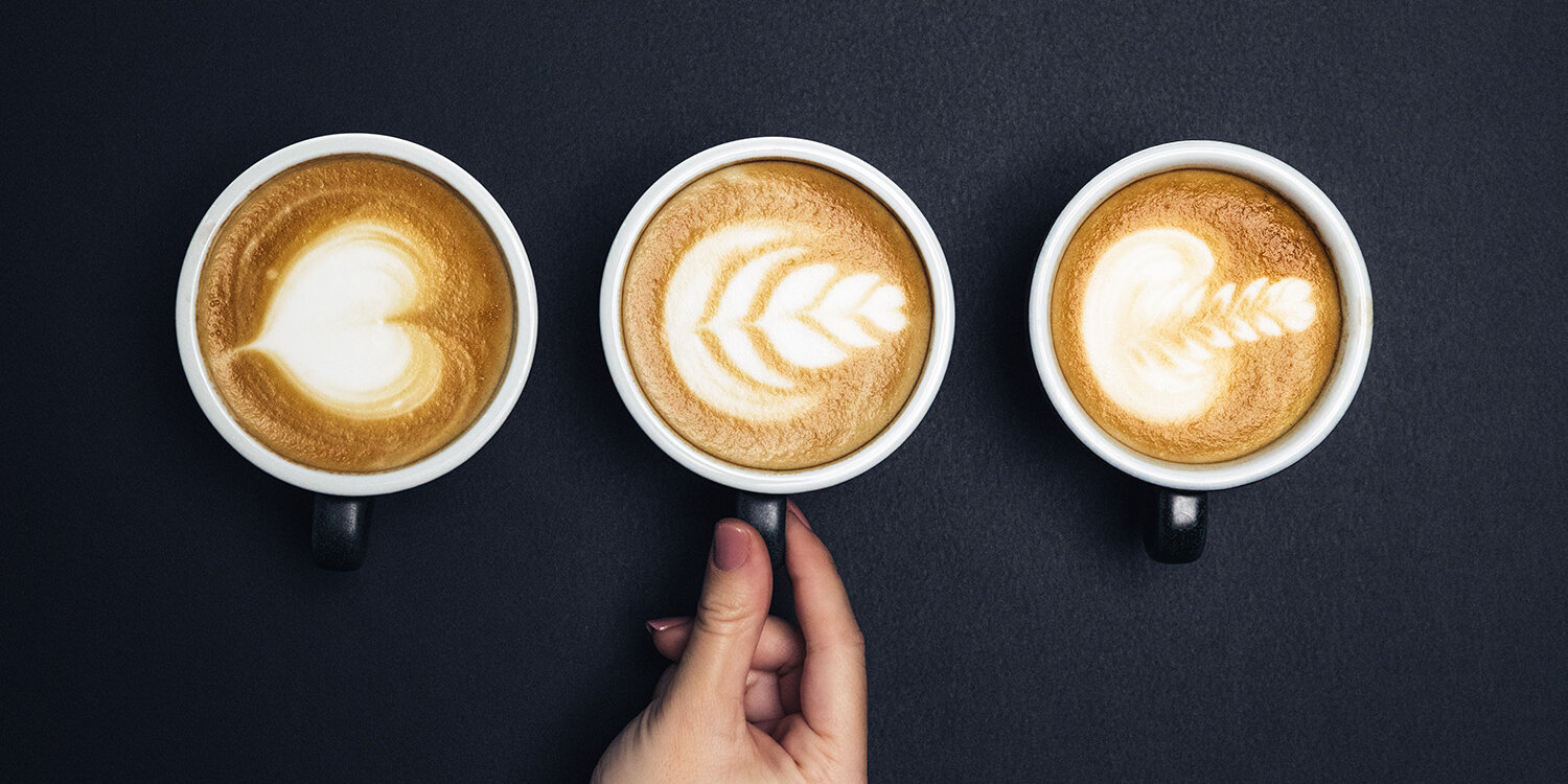 Hand greift Kaffeetasse mit Latte Art auf schwarzem Untergrund