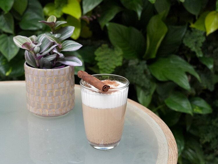 Kaffeegetränk mit Zimt und Blumen und Pflanzenwand im Hintergrund